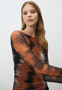 Langemouwen top met een abstract patroon in warme tinten van oranje, bruin en zwart. Gemaakt van een lichtgewicht, doorschijnende stof.