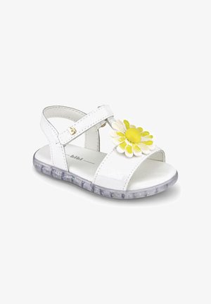 Biała sandałka dla malucha z paskiem na rzep, żółto-białą dekoracją stokrotki z przodu oraz przezroczystą podeszwą z błyszczącymi elementami.