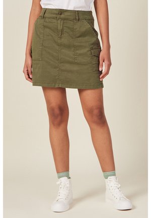 Spódnica bojówka z bawełny w kolorze oliwkowej zieleni z efektem wyblakłym, przednimi kieszeniami i szlufkami na pasek, zestawiona z białymi wysokimi trampkami i jasnymi zielonymi skarpetkami.