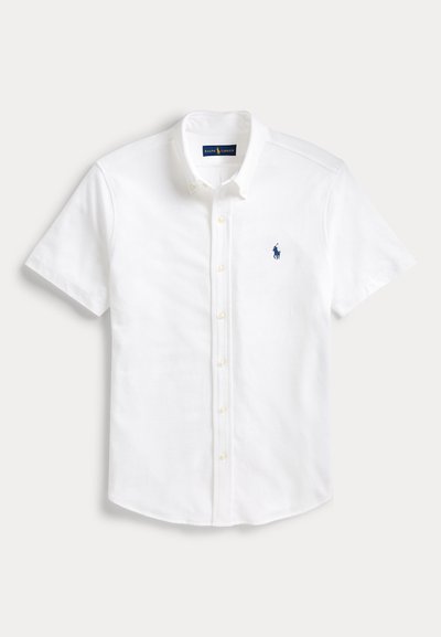 Camisa blanca de manga corta con botones, con cuello y un pequeño logo bordado en azul marino de un jugador de polo en el pecho izquierdo.