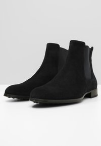 Schwarze Wildleder Chelsea-Stiefel mit elastischen Seitenpanels, einer glatten Sohle und einer runden Zehenpartie. Das Design ist schlank und minimalistisch.
