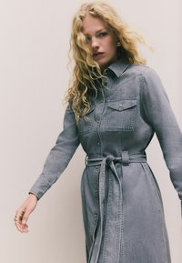 Denim-Hemdkleid in Hellgrau, mit langen Ärmeln, Knopfleiste, zwei vorderen Taschen, einem Taillengürtel und strukturiertem Stoff.