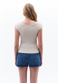 Top corto a maniche corte beige a coste abbinato a pantaloni shorts in denim blu a vita alta, con scollo curvo e design minimalista.