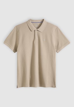 Beige kortærmet polo med krave og to-knaps slidse, lille logo på venstre bryst, lagt fladt på en lys baggrund.