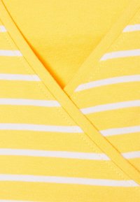 Žlutá tkanina s bílými vodorovnými pruhy a designem s přeloženým výstřihem do V, ukazující detailní prošívání a texturu.