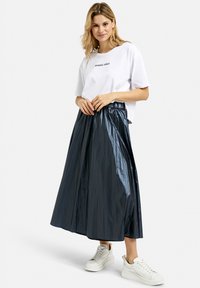 Metallic dunkelblaue Plisseerock bis zum Boden mit elastischem Bund, kombiniert mit einem weißen T-Shirt mit kurzen Ärmeln und Grafik sowie weißen Sneakers.