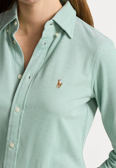 Camicia verde chiaro con colletto realizzata in tessuto testurizzato, dotata di bottoni perle e di un piccolo logo di cavallo ricamato sul lato sinistro del petto.