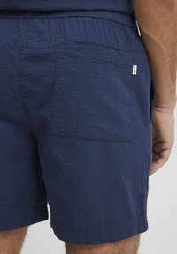 Dunkelblaue, strukturierten Shorts mit sichtbarem Gesäßtasche und elastischem Bund. Verfügt über ein kleines Markenetikett in der Nähe der Taschennähte.