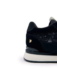 Zapatillas de ante negras con detalles de malla, que presentan una suela blanca y un logo en acento dorado. Tacón redondeado con un collar acolchado para mayor soporte.