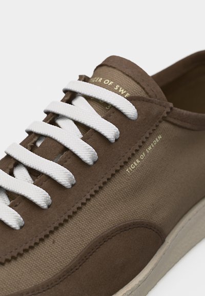 Ruskeat ja beiget lenkkitossut, joissa on valkoiset nauhat, kangas- ja mokkanahkapintaa sekä "Tiger of Sweden" -merkintä sivussa ja kielen kohdalla.