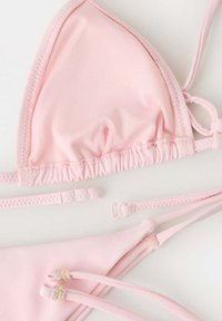 Haut et bas de bikini triangle rose clair avec bretelles ajustables et détails en perles sur la pièce du bas, posés à plat sur fond blanc.