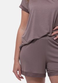 Completo di abbigliamento da casa in un morbido tessuto marrone tenue; top svasato con maniche arrotolate e shorts abbinati con un delicato accento sul bordo.