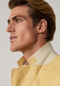 Veste en lin jaune clair avec un col clair en contraste, présentant un design de col structuré et des détails de couture visibles.