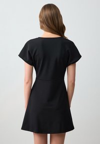 Schwarzes Kleid mit kurzen Ärmeln, figurbetontem Oberteil und schwingendem Rock. Hergestellt aus glattem Stoff, mit einem klaren, minimalistischen Design.