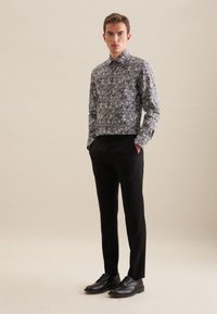 Czarna, kwiatowa koszula z długim rękawem z zapięciem na guziki, noszona z czarnymi spodniami i czarnymi butami, stojąca na neutralnym tle.