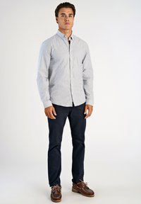 Ριγέ πουκάμισο με κουμπιά σε μπλε και λευκό, μακριά μανίκια, σε συνδυασμό με σκούρο ναυτικό παντελόνι και καφέ παπούτσια τύπου boat με κορδόνια και λαστιχένιες σόλες.