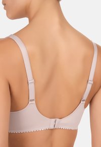 Lysbeige bh med bølget trim, justerbare stropper og en hægte- og øje-lukning bagpå. Glat stof og subtile design detaljer.