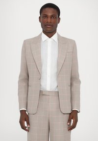 Completo grigio chiaro con un sottile motivo a quadri rosa, caratterizzato da un rever a punta, chiusura con bottone singolo e vestibilità su misura. Abbinato a una camicia bianca.