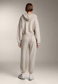 Felpa grigia chiara con una vestibilità comoda e cappuccio, abbinata a pantaloni della tuta a gamba affusolata con tasca posteriore e polsini elasticizzati.