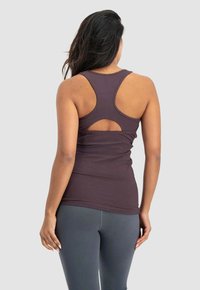 Brun ärmlös linne med racerback-design, med en öppen utskärning på ryggen. Mjuk tyg med en figurnära passform, kombinerat med grå leggings.