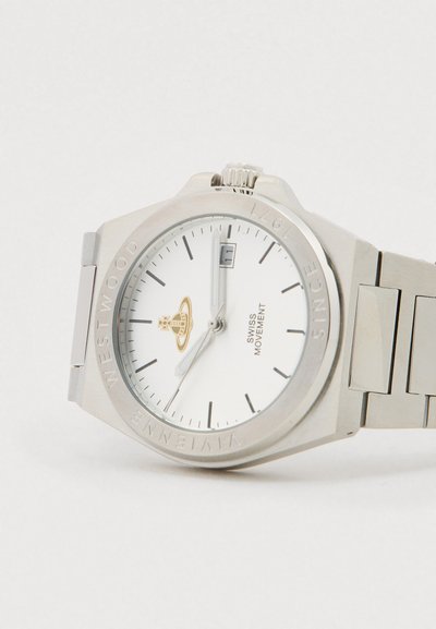 Sudraba krāsas nerūsējošā tērauda rokas pulkstenis ar baltu ciparnīcu, melniem stundu rādītājiem, datuma logu plkst. 3 un Vivienne Westwood logotipu zem plkst. 12.