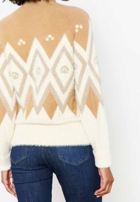 Pull en tricot crème et beige avec un motif en losange et une finition texturée. Associé à un jean bleu foncé.