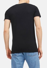 T-shirt nera a maniche corte con collo tondo, tessuto morbido, design aderente e orlo dritto, abbinata a jeans in denim azzurro chiaro.