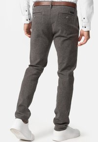 Szare materiałowe spodnie w wąskim kroju, z kieszeniami z tyłu, brązowym paskiem i białymi sneakersami. Skoncentrowano się na materiale i minimalistycznym designie.