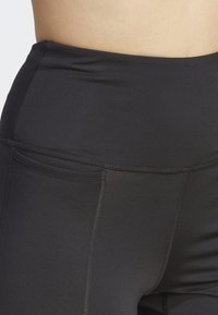 Svarte high-waisted leggings laget av elastisk materiale med flatlocksømmer og en jevn tekstur. Har en diskré sidelomme.