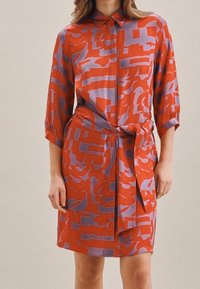 Vestido camisería de estampado rojo y lavanda con cuello, mangas de tres cuartos y cintura ajustada. Tejido suave con un diseño gráfico audaz.