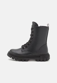 Bottine noire en matière synthétique lisse, dotée d'un devant à lacets, d'une semelle épaisse en caoutchouc et d'un détail de logo sur le talon.