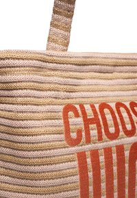 Vävd toteväska med växlande ljusrosa och beige ränder, med fet röd text som säger "VÄLJ" på ena sidan. Texturerat material.