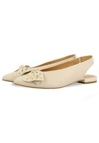 Bailarinas beige con tira al tobillo y punta afilada, que presentan un lazo decorativo con tachuelas doradas, textura suave y un bajo tacón bloque.