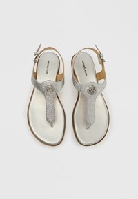 Ασημένια σανδάλια φλατ με γκλίτερ και μεταλλική λάμψη, με ρυθμιζόμενο λουρί στον αστράγαλο και στρογγυλή λεπτομέρεια με λογότυπο. Λείο εσωτερικό και υφασμένο λουρί.