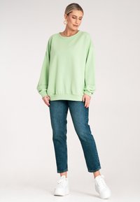 Jasnozielony oversize'owy sweatshirt z okrągłym dekoltem, ściągaczami na rękawach i u dołu, w połączeniu z ciemnoniebieskimi dżinsami i białymi sneakersami na platformie.