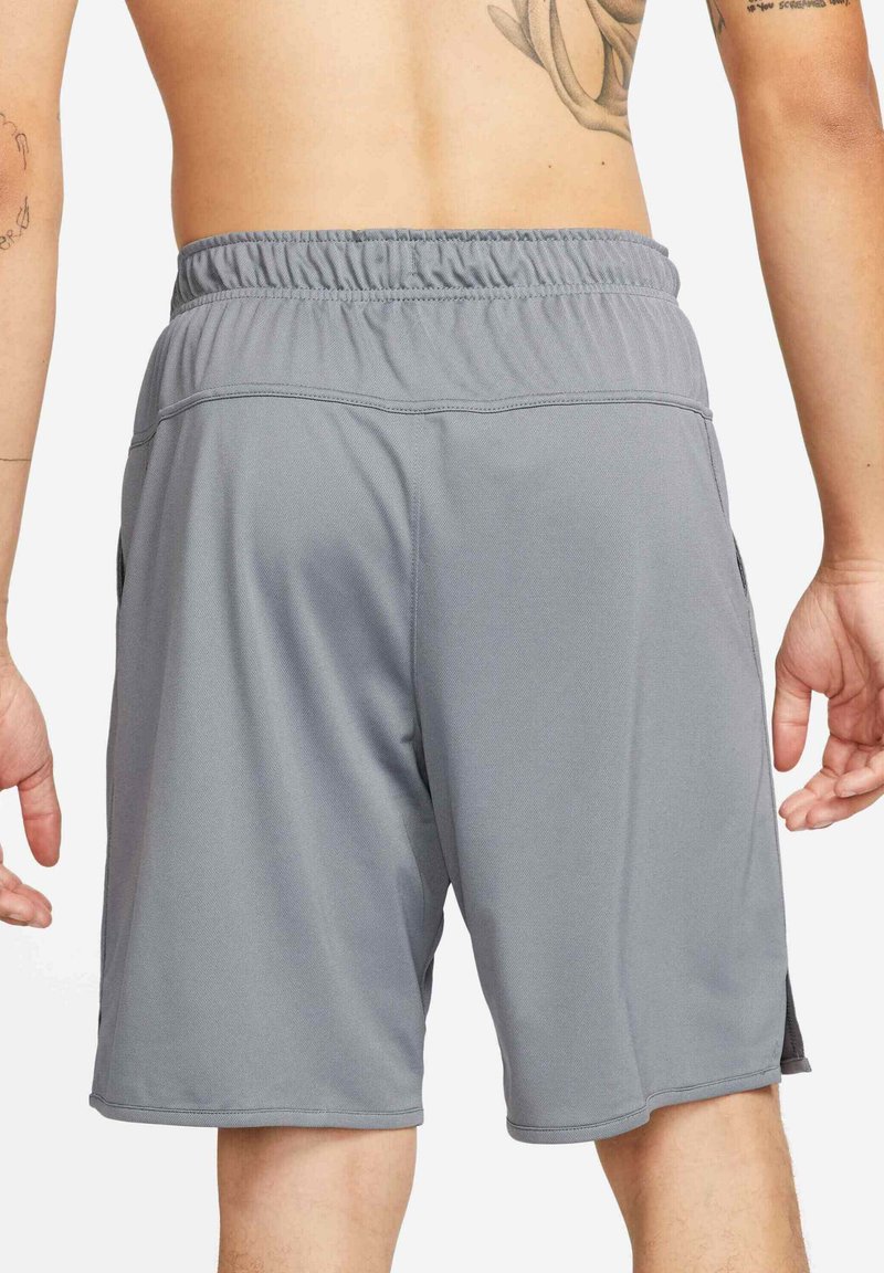 Vue de dos d'une personne portant un short de sport gris ample avec une taille élastique, montrant un dos nu et des bras tatoués.