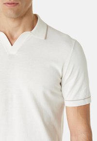 Polo en coton blanc avec un col V profond, des manches courtes et un fin liseré beige le long du col et des bordures des manches.