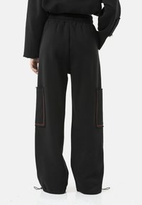 Zwarte, loszittende broek van zachte stof, met twee zijzakken met rode stiksel, een elastische tailleband en verstelbare zoom met trekkoord.