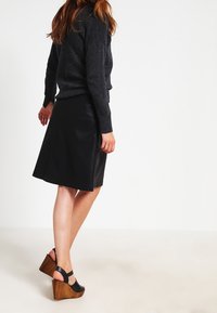 Zwarte leren rok, kniehoogte, gecombineerd met een donkergrijze trui. Heeft een effen kleur. Schoenen zijn zwart met een houten sleehak.