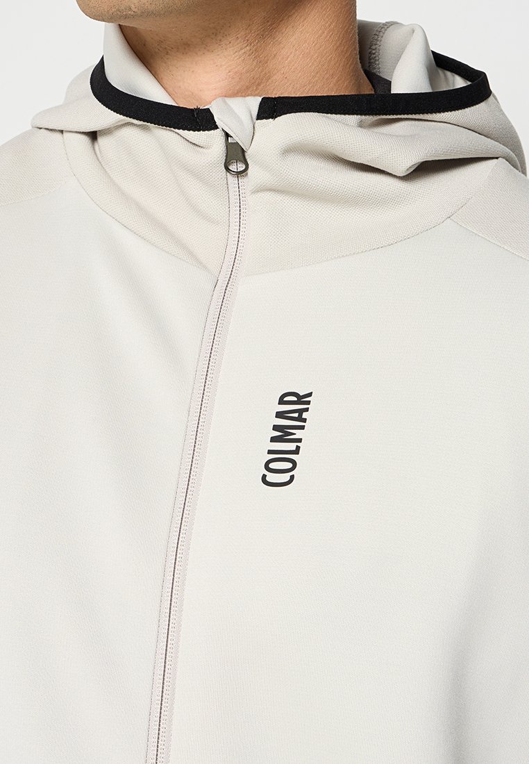 Felpa zip grigia chiara con bordi e logo neri. Presenta una texture morbida e un cappuccio regolabile, progettata per comfort e vestibilità.