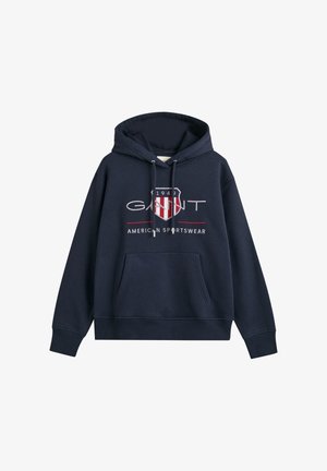 Granatowy hoodie wykonany z materiału mieszanki bawełny. Posiada kieszeń kangurką, kaptur ze sznurkiem oraz logo z tarczą w czerwono-białe paski.