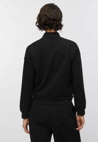 Must musta dressipluus, millel on kõrge krae, lai lõige, soonikkäised ja -ääris, tehtud pehmest ja siledast materjalist.