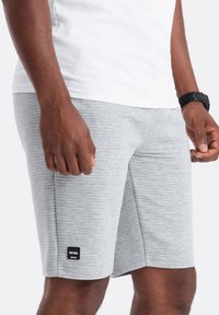 Shorts de sport gris à rayures, avec une coupe mi-longue, comportant une petite étiquette noire sur le côté gauche et un tissu lisse et texturé.
