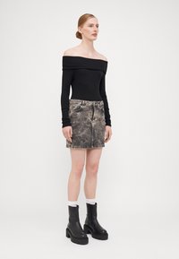 Svart off-shoulder ribbestrikket topp kombinert med en falmet denim mini skjørt med stjernemønster, komplementert av kraftige svarte lærstøvler.