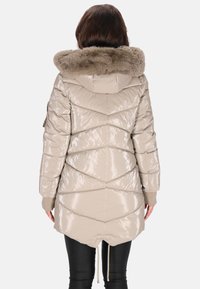 Bézs színű, fényes felületű puffertöltött dzseki, műszőrmével bélelt kapucnival, cikkcakk steppelt mintával és állítható derékkal, húzózsinórral.