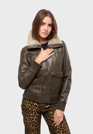 Veste bomber en cuir marron avec un col en fourrure beige, des poignets côtelés et deux poches avant. Portée par-dessus un pantalon à imprimé léopard.