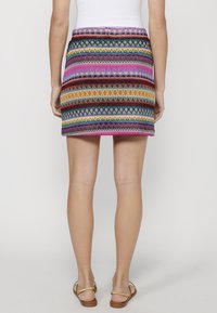 Večbarvna patterned krila z geometrskimi vzorci; ima prilega pas in zaključek, ki konča nad kolenom. Narejeno iz tkanine.