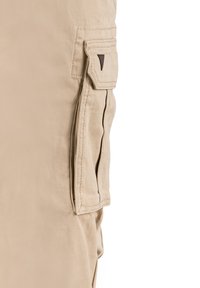 Beige cargo-housut, jotka on valmistettu kestävästä kankaasta, ja niissä on kyljessä läpällä varustettu tasku sekä kontrastivärisiä tummia yksityiskohtia.