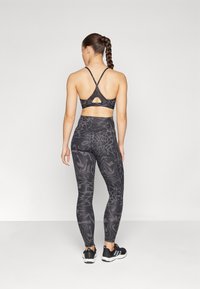 Reggiseno sportivo nero con spalline incrociate, abbinato a leggings a vita alta con un motivo vorticoso. Entrambi hanno una texture liscia ed elastica.