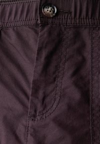 Tissu violet foncé avec une texture lisse, présentant un détail de bouton et des coutures sur le côté. Gros plan sur le design de pantalons ou de shorts.